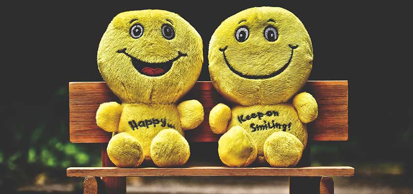 Two emoji stuffed dolls on a bench.
