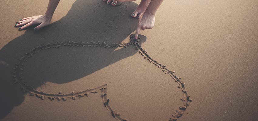 A woman drawing a heart in sand.