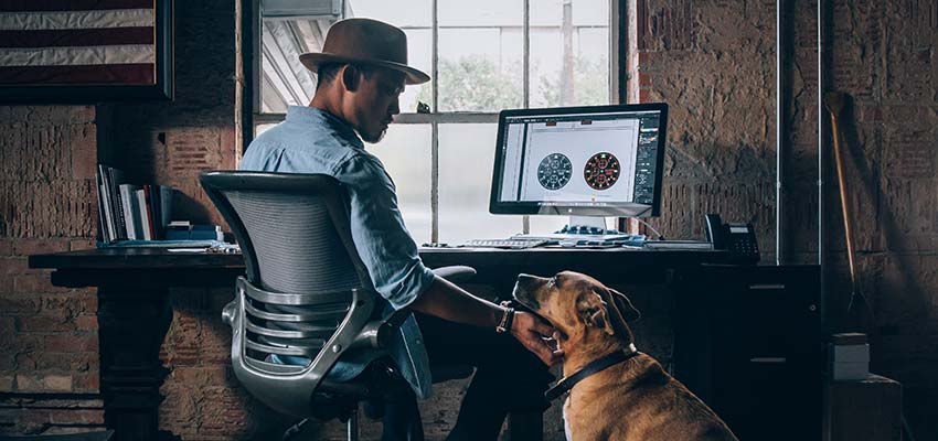 Man sitting at a computer, petting a dog.