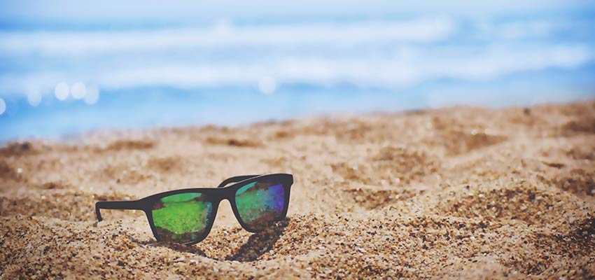A pair of sunglasses sitting on a sandy beach.