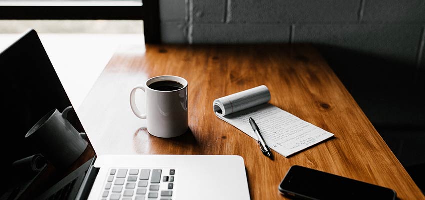 A table with a laptop computer, notepad and phone.